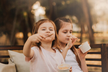 Little girl eating ice cream in summer park and looking at camera. Cute baby walking outdoors enjoy sweet dessert.