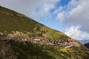 Large Tibetan monastery complex on a hillside under blue and cloudy sky in Sichuan province