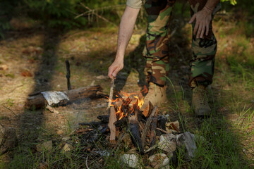 Man in military clothes is making campfire in the woods. The concept of adventure, travel, tourism, camping, survival and evacuation.