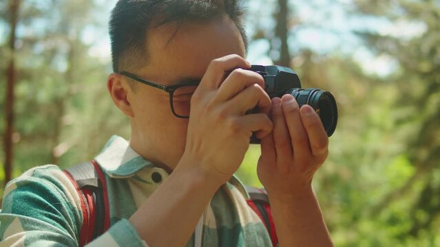 Asian man taking photo in forest, tourist photographer using camera , safe travel and explore, walking hiking tours. Traveling and hiking alone. Summer tourism, wild nature. 