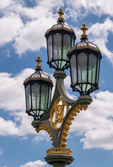 Fototapeta na wymiar London, UK - July 4, 2022: Lantern closeup on Westminster bridge against blue cloudscape, triple light and golden decorations.