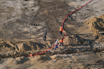 Workers at a construction site laying a cable in a trench dug in the ground, top view