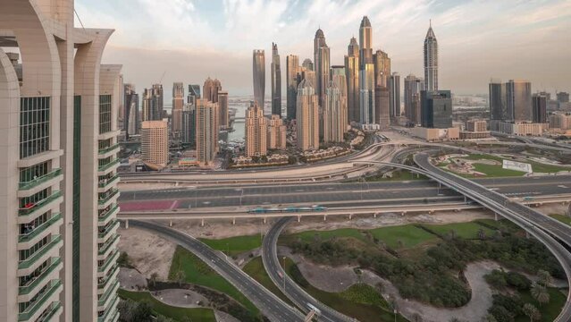 Panorama of Dubai Marina highway intersection spaghetti junction night to day transition timelapse. Illuminated tallest skyscrapers on a background. Aerial top view from JLT district before sunrise