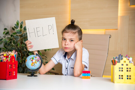 Sad tired frustrated boy sitting at the desk at school with globe and pencils holding paper with word Help. Learning difficulties, education concept. holding a sign help 