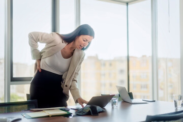 Businesswoman woman standing by the desk in the office and having back pain