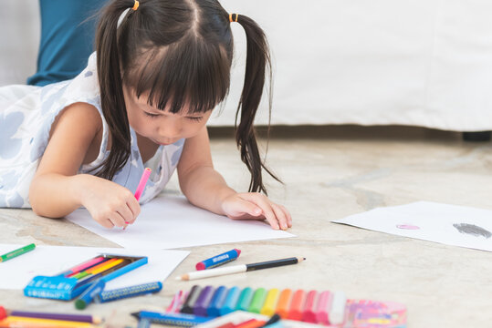 A 3 year old Asian baby girl Lying on the floor, are concentrating make art by using colored pencils, concept to children and education online.	