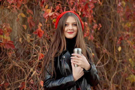 Beautiful stylish young woman in black leather jacket standing and posing in autumn park on red leaves background in fall