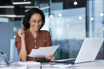Young beautiful Arabic business woman working in modern office with documents, paperwork, reading report and smiling happy with result