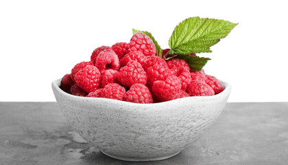 Bowl of fresh ripe raspberries with green leaves on grey table against white background