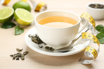 Cup of diet herbal tea, measuring tape and dried leaves on wooden table