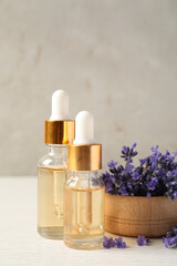 Bottles of essential oil and lavender flowers on white wooden table