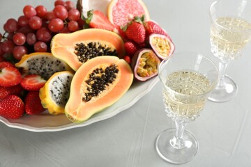 Delicious exotic fruits and glasses of wine on light grey table