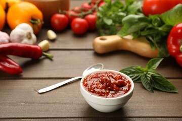 Delicious adjika sauce in bowl and ingredients on wooden table