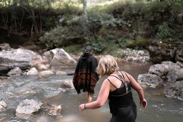 A couple is crossing a river getting their barefoot feet wet