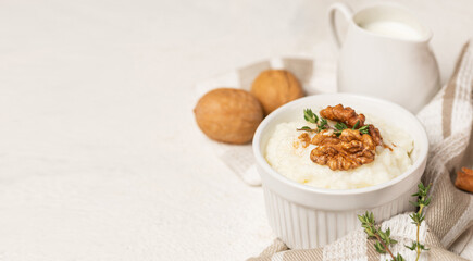 White rice pudding mold, milk or cream in creamer, cinnamon, whole walnuts and thyme on  white textured background. Serving a traditional healthy dessert