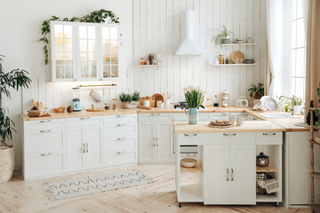 Modern white Scandinavian style kitchen with a wooden worktop filled with kitchen accessories. Stylish kitchen interior with large windows and potted plants. Empty space