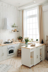 Modern white Scandinavian style kitchen with a wooden worktop filled with kitchen accessories. Stylish kitchen interior with large window and potted plants. Nobody