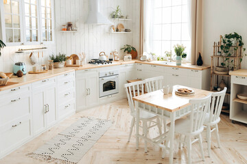 Modern white Scandinavian style kitchen with a wooden worktop filled with kitchen accessories. Stylish kitchen interior with wooden dining table, large windows and potted plants. Empty space