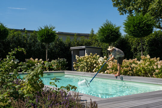 Mann mit Strohhut reinigt an einen Sommertag den Pool mit dem Kescher.