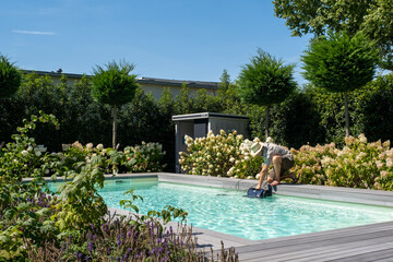 Mann mit Strohhut am Pool im Sommer, reinigt  den Poolroboter.