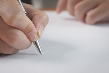 Closeup of businessman hand holding pen and singing a signature on paper. Business contract...