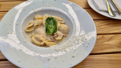 pasta with cheese and vegetables on a white plate at restaurant, eating out, way of serving food 