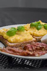 fresh scrambled butter eggs with bacon, pepper and basil on green plate on steel black table 