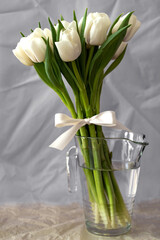 white tulips in the glass vase filled with water with the bow in front of gray paper background 