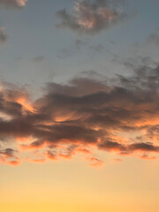 Dramatic sunset landscape with puffy clouds lit by orange setting sun and blue sky.