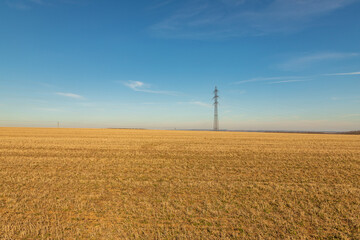 High voltage poles for electricity distribution in the countryside. In the background is a blue sky with dramatic clouds.