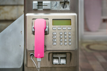 Public pay phone made of scratched metal with a pink handset, insert for coins and credit card, in...