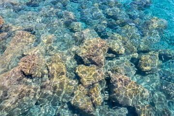 Rippled transparent aquamarine sea water surface with yellow rocks underwater