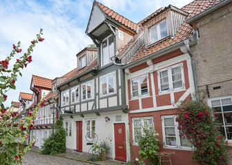 Fototapeta na wymiar Historic half-timbered houses in the old town of Flensburg, Germany, on a narrow cobblestone alley with flowers on the facades, tourist attraction, selected focus
