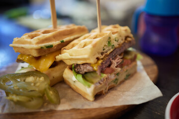 Waffle sandwich with meat, cheese, sauce and vegetables on wooden table background.