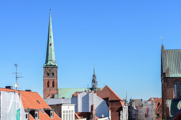 Obraz premium St. Jakobi church with clock tower and ridge turret behind the roofs of the old town of Luebeck, Germany under a blue sky, copy space