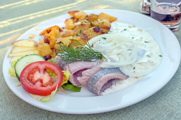 Pickled herring or matjes fillet with cream sauce and onions, served with fried potatoes and salad...