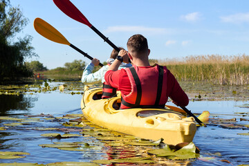 Rear view on couple Man and a woman paddle yellow kayak on a river among the green lilies at summer
