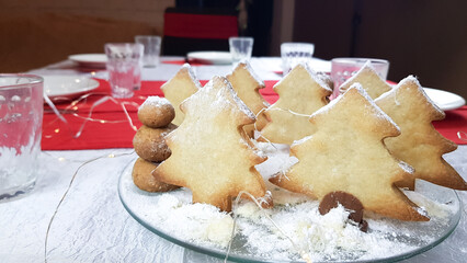 Christmas cookies in the form of Christmas trees decorated with powdered sugar on a round plate