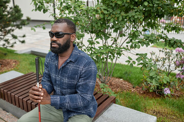High angle portrait of blind man wearing sunglasses and holding cane in braille while sitting on...