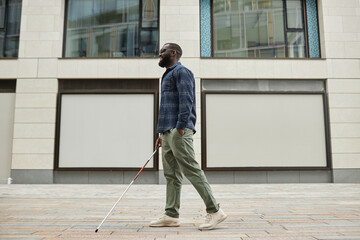 Full length portrait of smiling blind man walking in city and using cane, copy space