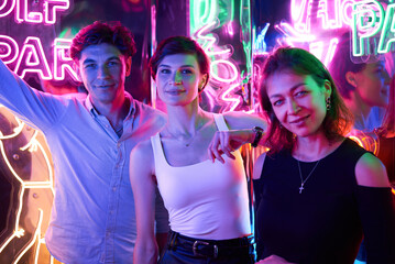 Image of two beautiful women and one man in an amusement park in a room with neon light....
