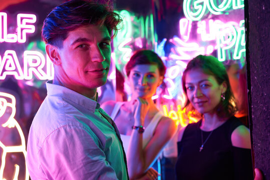 Image of two beautiful women and one man in an amusement park in a room with neon light. Entertainment concept.