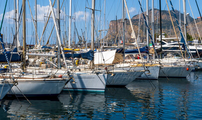 boats and yachts on pier in marine city port with masts and bulidings and blue sky on background