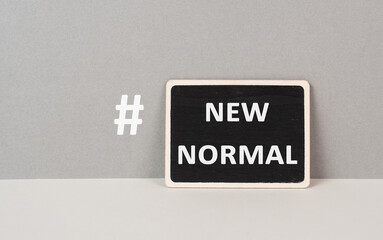 The words new normal with a hashtag are standing on a chalkboard, gray colored background
