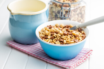 Breakfast cereal flakes in bowl and milk on checkered napkin.