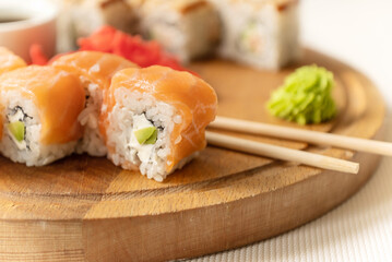 Pieces of fresh salmon philadelphia sushi roll served with wasabi cream and chopstick on wooden board and ready to eat