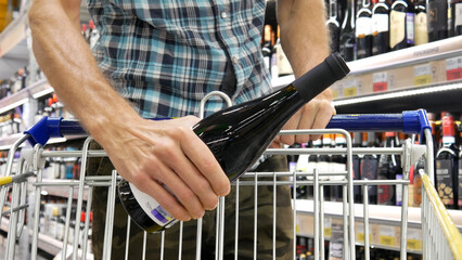 Close-up of a shopping trolley in alcohol department and a man puts a beautiful bottle of wine into it