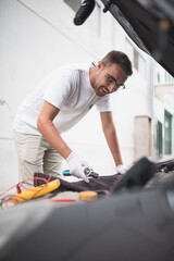 Mecánico joven arreglando un coche felizmente. Joven mecánico feliz con su trabajo.