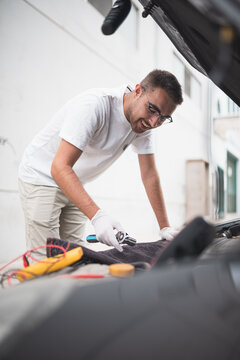 Mec&aacute;nico joven arreglando un coche felizmente. Joven mec&aacute;nico feliz con su trabajo.