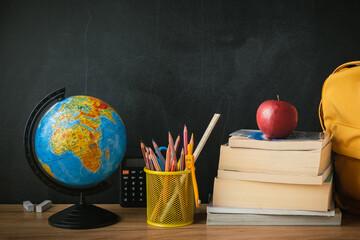 School supplies next to the globe and stack of books on the blackboard background. Back to school concept on September day